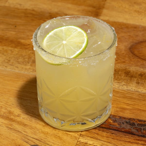 A S/T Hooligans margarita with a salted rim and lime wedge on a wooden table.