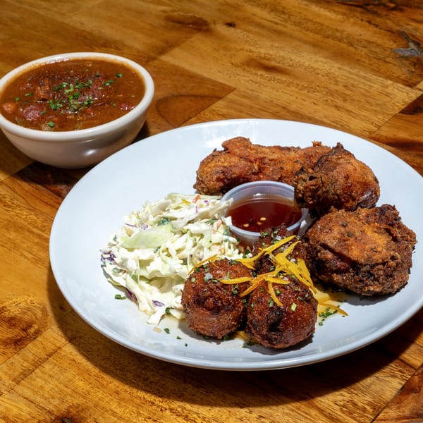 Creole fried chicken, hush puppies, coleslaw, and a bowl of gumbo on a wooden table.