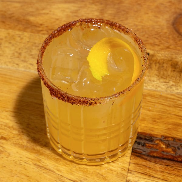 A creole cocktail with a spiced rim and lemon peel garnish on a wooden table.