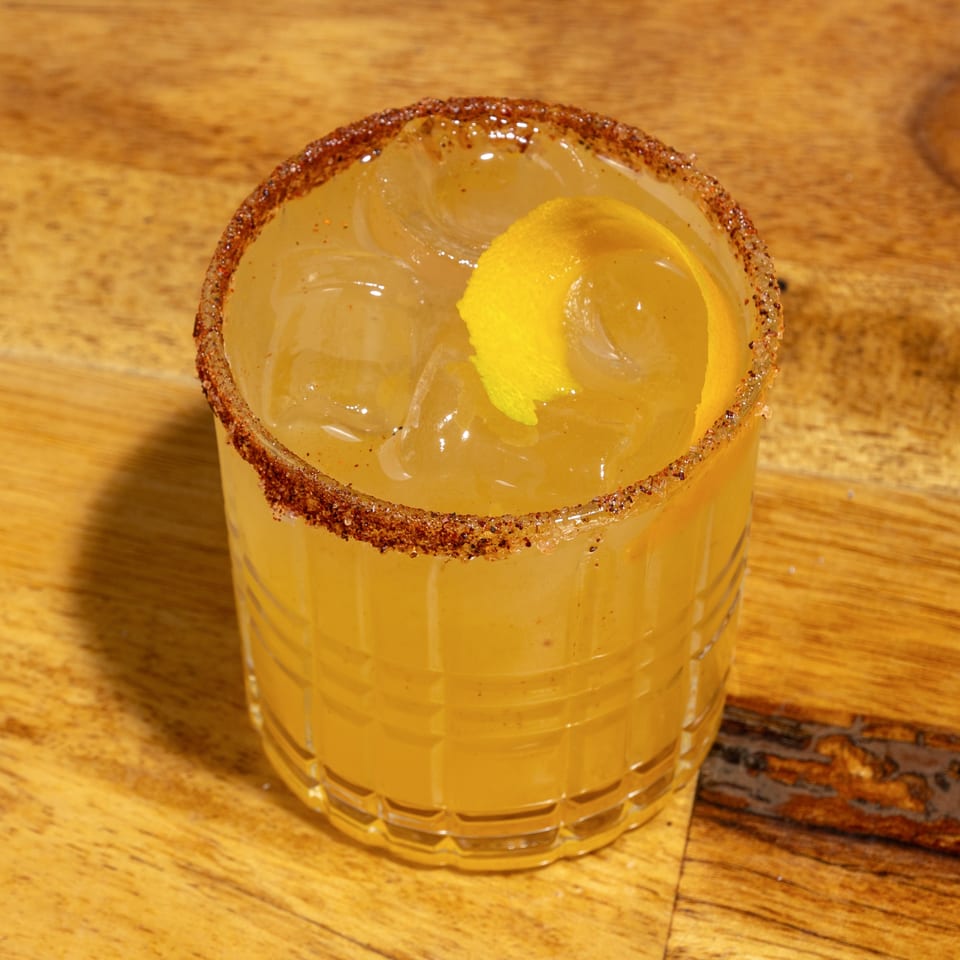 A creole cocktail with a spiced rim and lemon peel garnish on a wooden table.