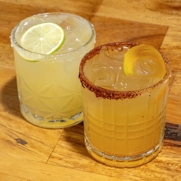 Two cocktails, one with a lime and salt rim, the other with a lemon peel and spiced rim.