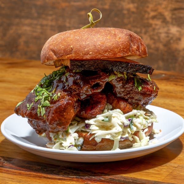 A large Creole BBQ sandwich with coleslaw and cilantro on a white plate.