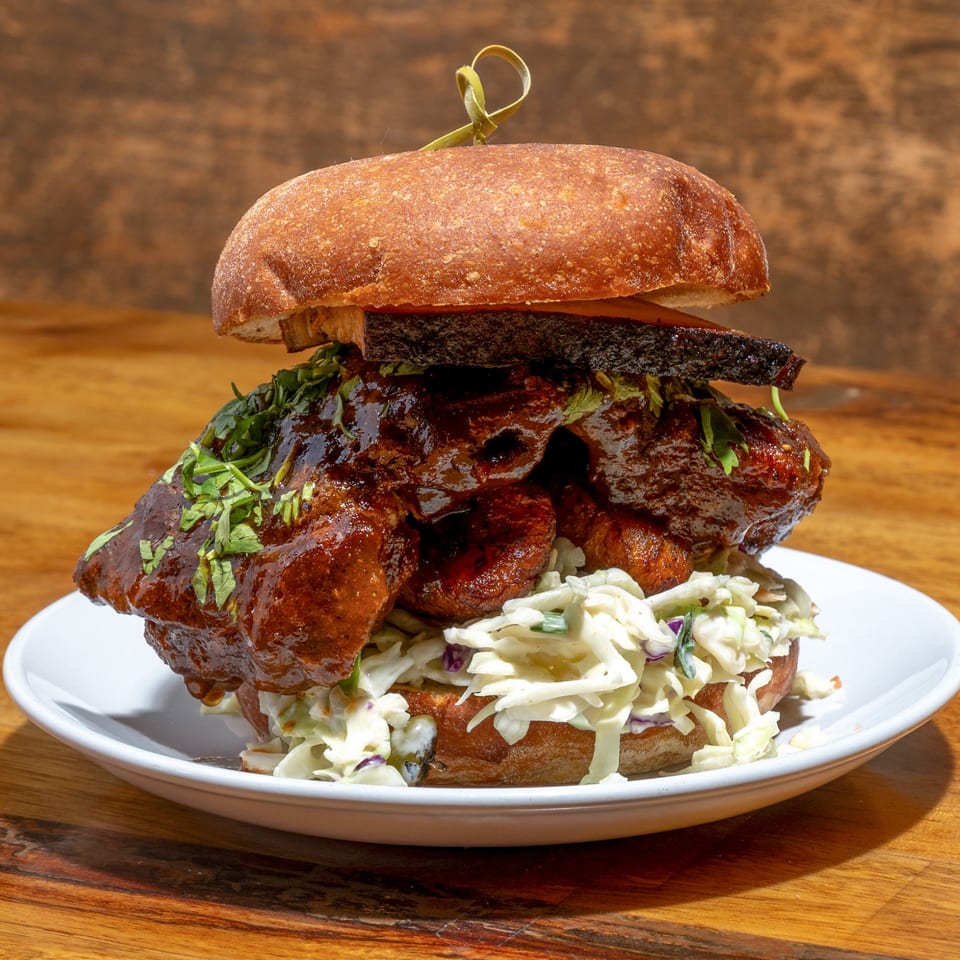 A large Creole BBQ sandwich with coleslaw and cilantro on a white plate.